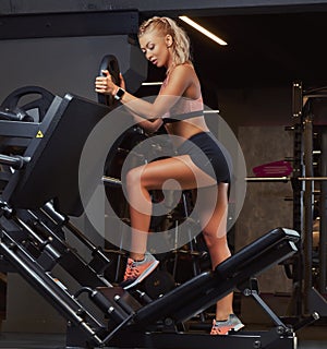 Beautifull fitness woman in sportswear posing near the legs press machine in a gym.