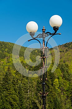 A Beautifully Crafted Street Lamp Facing the Blue Sky and Green Mountains