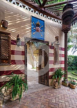 Beautifully crafted wooden door opens to a courtyard with red and white striped wall, wooden columns and plant pots