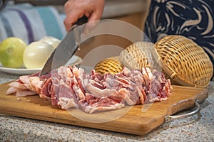 Beautifully cut slices of fresh fatty meat for further cooking on a background of bamboo utensils and vegetables.