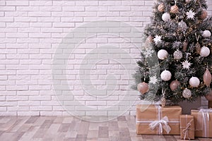 Beautifully decorated Christmas tree and gift boxes near white brick wall, space for text