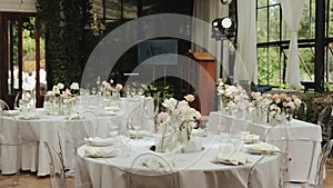 Beautifully decorated room with tender floral compositions on tables and plastic transparent chairs for romantic wedding