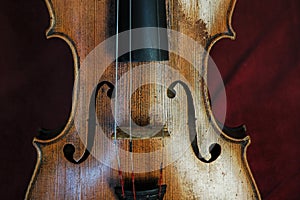 Beautifully designed old violin with missing strings set against a burgundy red velvet background