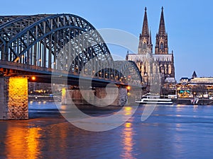 The beautifully illuminated cathedral in the German city of Cologne and the Hohenzollern Bridge over the river Rhine at dawn