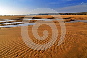 Beautifully patterened and water riven wet sand reflecting blue sky