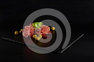 Beautifully served prosciutto or jamon on a black slate board.