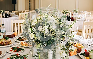 Beautifully set round tables at the restaurant. Delicious food at the wedding reception. White tablecloths and flowers decorations