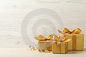 Beautifully wrapped gift boxes and confetti on white wooden table, space for text