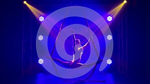 Beautiiful silhouette of female aerial gymnast performing an aerial acrobatic twine on silks in a studio. Performance in