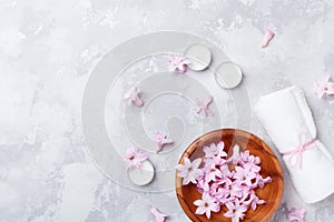 Beauty, aromatherapy and spa background with perfumed pink flowers water in wooden bowl and candles on stone table. Flat lay.