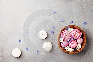 Beauty, aromatherapy and spa background with perfumed water with flowers in wooden bowl and candles on stone table. Top view, flat