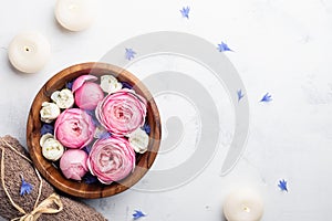 Beauty, aromatherapy and spa background with perfumed water with flowers in wooden bowl, towel and candles on stone table.Top view