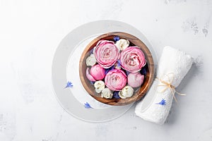 Beauty, aromatherapy and spa background with perfumed water with flowers in wooden bowl and towel on stone table. Top view, flat l