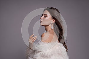 Beauty art portrait of a beautiful woman with long hair, white fur coat with long faux fur. Beautiful earrings in a woman`s ears.