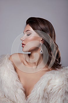 Beauty art portrait of a beautiful woman with long hair, white fur coat with long faux fur. Beautiful earrings in a woman`s ears.