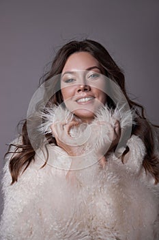 Beauty art portrait of a beautiful woman with long hair, white fur coat with long faux fur. Beautiful earrings in a woman`s ears.