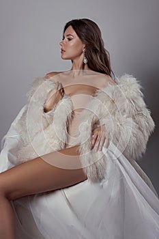 Beauty art portrait of a beautiful woman with long hair, white fur coat with long faux fur. Beautiful earrings in a woman`s ears.