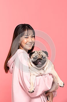 Beauty Asian young woman holding dog pug breed on her arm smile and happiness,Owner hug her cute pet dog with love on pink