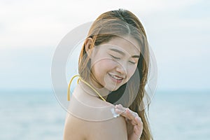 Beauty Attractive Asian young woman  smile with healthy skin applying sunscreen lotion on her shoulder on the beach