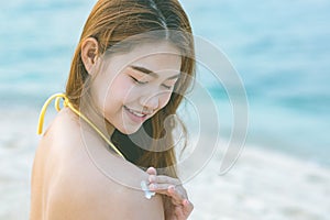 Beauty Attractive Asian young woman smile with healthy skin applying sunscreen lotion on her shoulder on the beach