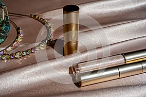 Beauty background with facial cosmetic products and hair hoop with stones. Glitter lipstick tubes on beige silk