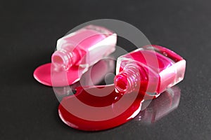 Beauty background two bottles of nail polish bottles red or burgundy pink spill poured on the table on a black background close-up