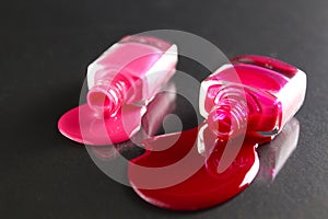 Beauty background two bottles of nail polish bottles red or burgundy pink spill poured on the table on a black background close-up