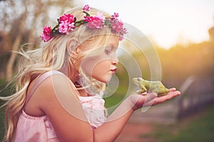 Beauty and the beast. a cheerful little girl holding a frog and going in for a kiss while standing outside in nature.