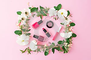 Beauty blogger desk with cosmetics, lipstick, eye shadows, nail polish and pink frame of flowers on pink background. Flat lay, top