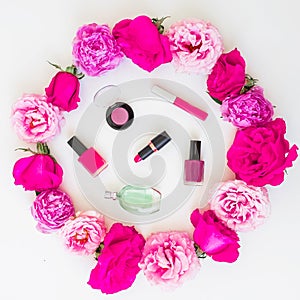 Beauty blogger desk with cosmetics - lipstick, eye shadows, nail polish and pink frame of roses on white background. Flat lay, top