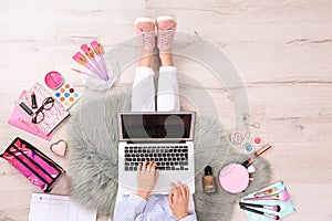 Beauty blogger with laptop and cosmetics sitting on floor