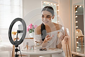 Beauty blogger with makeup product recording video in room at home. Using ring lamp and smartphone