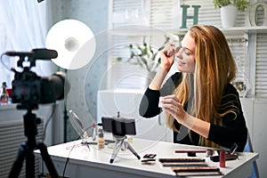 Beauty blogger woman filming daily make-up routine tutorial at camera on tripod. Influencer girl live streaming photo