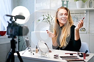 Beauty blogger woman filming daily make-up routine tutorial near camera on tripod. Influencer blonde girl live streaming