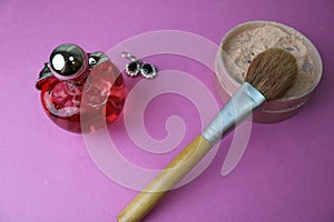 Beauty box, powder with a brown brush from nap for makeup, pink perfume and earrings on a background. Flat lay. Top view