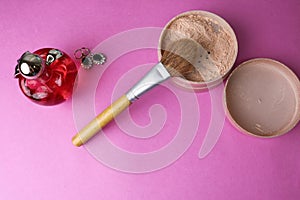 Beauty box, powder with a brown brush from nap for makeup, pink perfume and earrings on a background. Flat lay. Top view