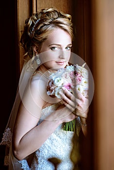 Beauty bride in bridal gown with bouquet and lace veil indoors