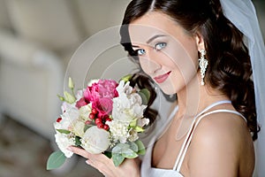 Beauty bride in bridal gown with bouquet and lace veil indoors