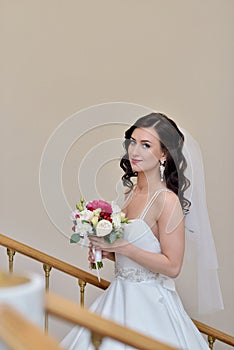 Beauty bride in bridal gown with bouquet and lace veil indoors
