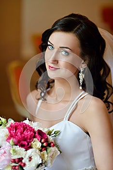 Beauty bride in bridal gown with bouquet and lace veil indoors