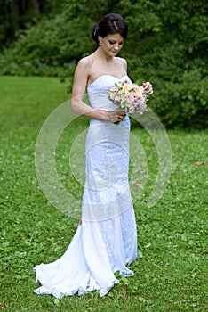 Beauty bride in bridal gown with bouquet and lace veil in the nature