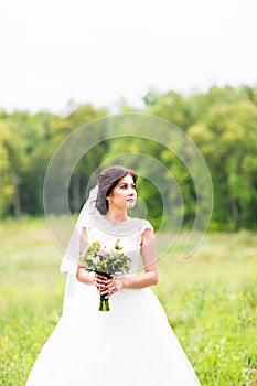 Beauty bride in bridal gown with bouquet and lace veil on the nature. Beautiful model girl in a white wedding dress