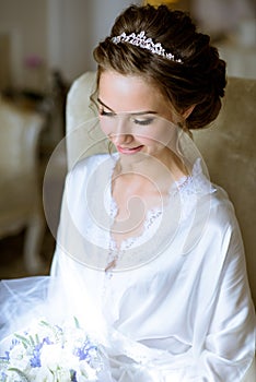 Beauty bride in dressing gown with bouquet indoors