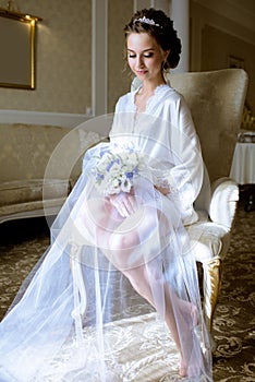 Beauty bride in dressing gown with bouquet indoors