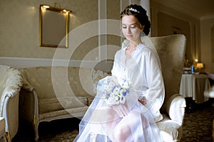 Beauty bride in dressing gown with bouquet indoors