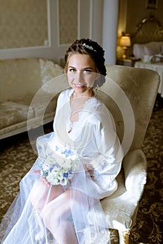 Beauty bride in dressing gown with bouquet indoors