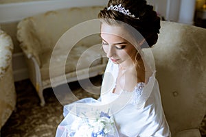 Beauty bride in dressing gown with bouquet indoors