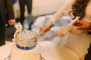 Beauty bride and handsome groom are cutting white wedding cake decorated with blue riband