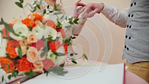 Beauty bride and handsome groom are wearing golden rings each other in front of wedding bouquet. Marriage ceremony.