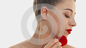 Beauty and bright red lipstick on lips. Pretty woman holds a red rose petal on her cheekbone. Profile of young light